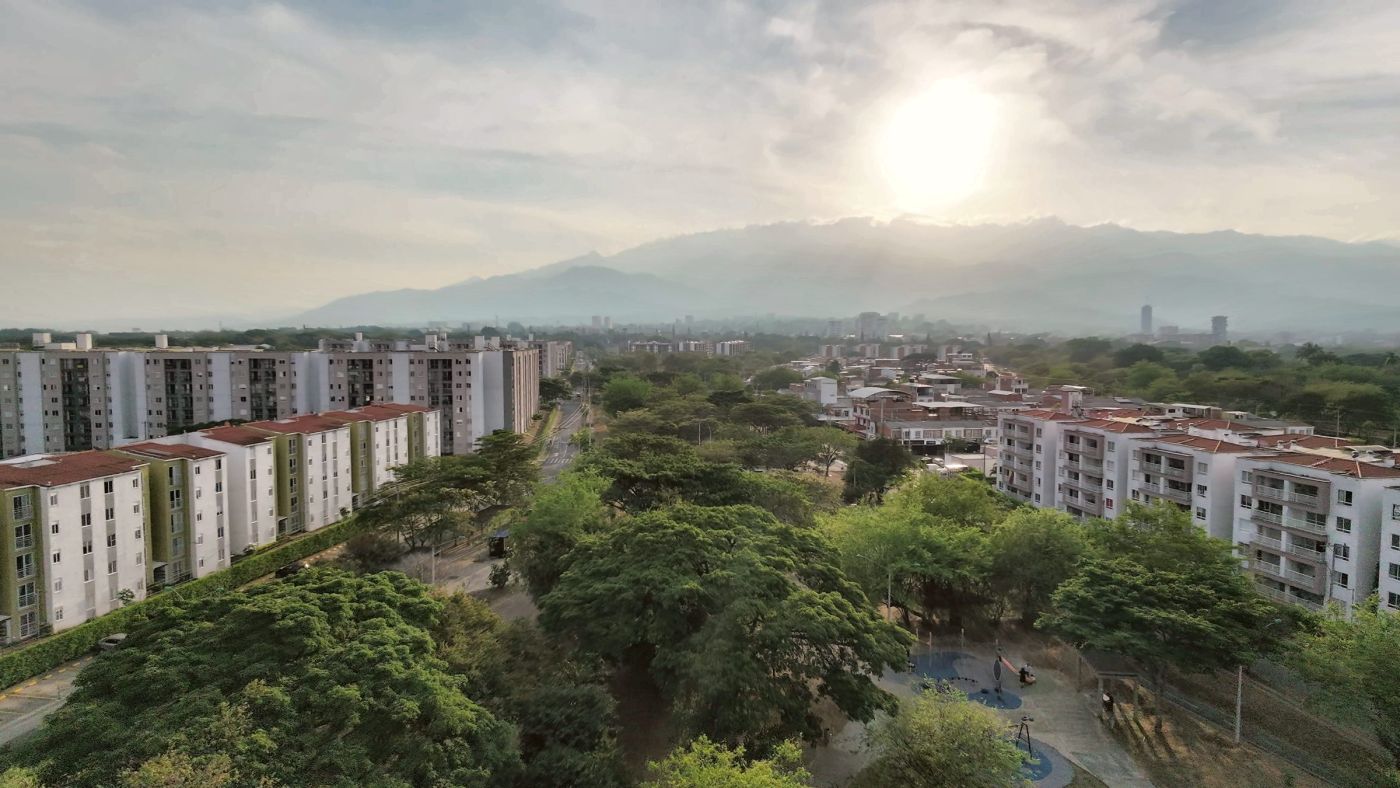 Edificios y árboles al atardecer con el sol sobre las montañas de Cali